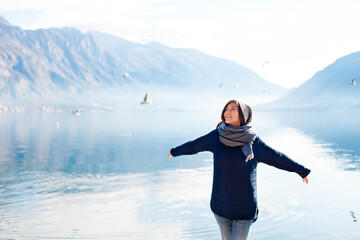 Happy young woman has fun at winter sea beach with flying seagulls.