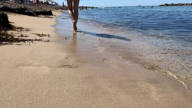Woman barefeet walk along sand beach, Hot sunny weather, clear ocean water, Freedom life escape from city, summer vacation, breeze wind blowing pants, slow motion