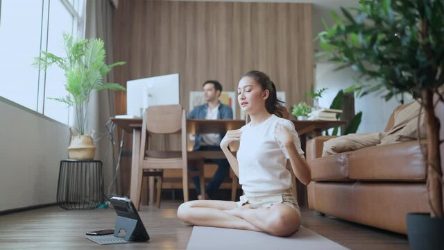 young asian female wife train yoga exercise workout practicing from online study lesson at living room,couple wroking from home caucasian man working with paper chart desktop pc at home
