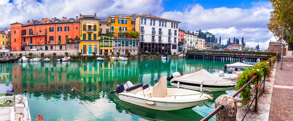 Fototapeta na wymiar Idyllic lake scenery - tranquil beautiful village (town) Peschiera del Garda with fishing boats and colorful houses. Lago di Garda, northern Italy