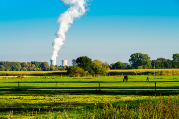 Blick auf Atomkraftwerk, AKW, Gundremmingen, mit blauem Himmel und hoher Rauchsäule eines Kühlturms, Wiesen und Felder im Vordergrund