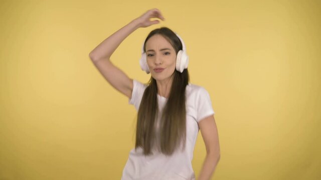 Funny attractive woman 35 years old middle age on yellow background in studio in profile. Woman fun dancing listening to music in large white wireless headphones