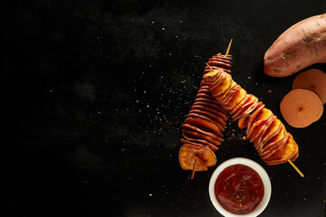 Fried tornado sweet potatoes served with spicy ketchup on black background with blank space
