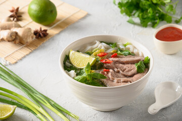 Pho Bo Soup with beef, rice noodles, ginger, lime, chili pepper in bowl on white backgound. Close up. Vietnamese and Asian cuisine.