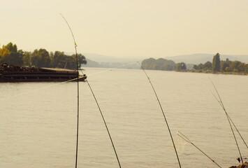 Einige Angelruten am Ufer des Rheins mit einem Lasttanker im Hintergrund