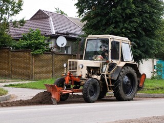 Cleaning the street from dirt using a tractor with a bucket.