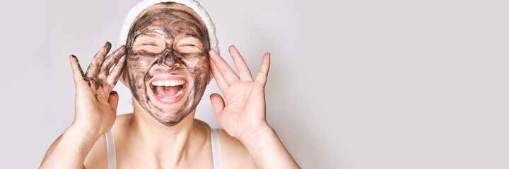 Young woman applying black face mask. Charcoal facial product. Acne and pimple removing. Mud coal...