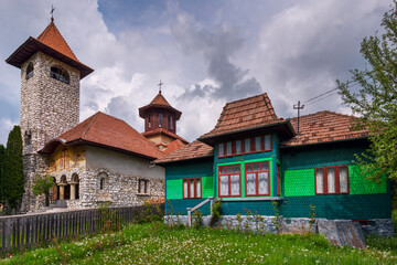 Fototapeta na wymiar Colorful wooden dwelling and vintage stone and wood Orthodox church with bell tower in the Romanian Carpathian Mountains of Transylvania