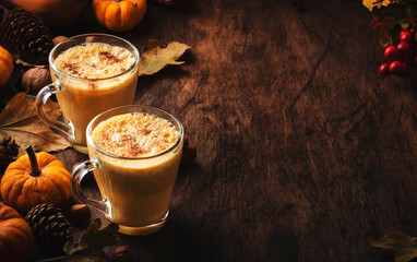 Pumpkin butter latte or coffee, keto drink on wooden table with fallen leaves, small pumpkins, pine...