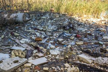 heaps of construction waste, household waste, foam and plastic bottles on the shore of a forest lake, environmental pollution problems