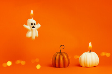 burning candles in the shape of a ghost and a pumpkin on an orange background. halloween, thanksgiving, harvest festival concept