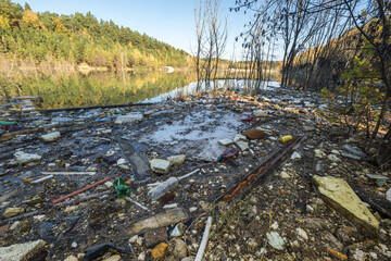 heaps of construction waste, household waste, foam and plastic bottles on the shore of a forest lake, environmental pollution problems