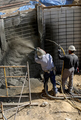 Construction workers shooting shotcrete to a waterproofed retaining wall