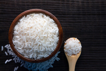 Top view of white rice in wooden bowl on  dark wooden table.