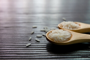 White rice in wooden spoon on dark wooden table. Selective focus.