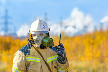 Firefighter rescuer in a protective suit and white helmet, fighting a fire at a chemical plant....