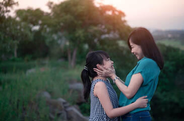 Mother and daughter are hugging and having fun outdoor in green nature with sunset