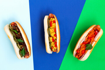 Hot dogs with different toppings: pickles, fried onion, tomatoes and carrots with green on a colour...