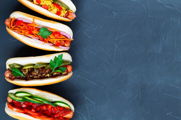 Hot dogs with different toppings: pickles, fried onion, tomatoes and carrots with green on a black background with copy space. flat lay. Fast food concept top view