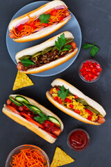 Different tasty homemade hot dogs with tomato, cucumber, onion, salad, carrots, spices and mustard, ketchup on a dark table with copy space. flat lay. Fast food concept top view.