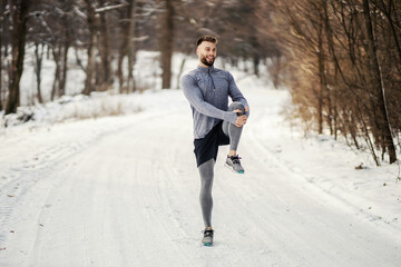 Sportsman doing stretching exercises and preparing to run in nature at snowy winter day. Winter fitness, sport, cold weather