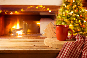 Wooden table with coffee cup over Christmas tree and fireplace background.  Christmas and New Year mock up for design and product display.