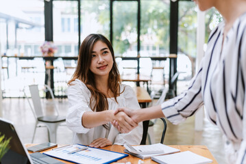 Image of happy Asian businesswoman success cooperation agreement handshake congratulation document graphing calculator laptop placed at the office.