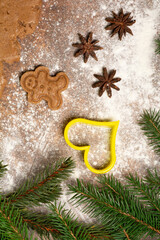 Gingerbread man cookie, three star anise fruits, heart-shaped cookie cutter, fir branches and a piece of rolled out gingerbread sweet dough are lying on a kitchen worktop sprinkled with flour.