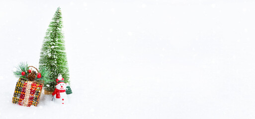 A Christmas tree, a gift box and a toy snowman on white natural snow in a snowfall. Decoration for New year and Christmas, greeting card with copyspace