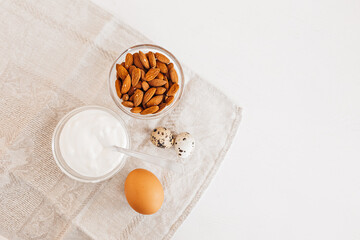 Nuts almonds, sour cream or yogurt, chicken and quail eggs on a linen kitchen towel on a white table. Healthy food and nutrients for proper nutrition of the brain and body concept