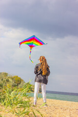 a girl launches a bright kite into the sky on the beach by the river. the concept of outdoor activities and a healthy lifestyle.