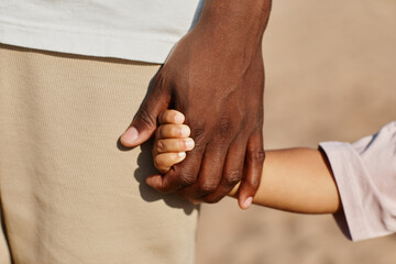Close up of father and son holding hands while enjoying walk on beach in sunlight, copy space