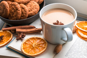 A large cup of coffee and a book near the window, several knitted blankets and slices of dried oranges remind of autumn, a cozy time and home holiday. Flat lay