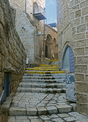 Fototapeta na wymiar An old narrow street in old Jaffa paved with paving stones with houses with walls of large stone and arched openings