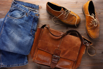 Denim jeans and old boots with leather bag at wood table. Travel concept as retro clothes