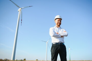 Engineer is checking energy production on wind turbine. Worker in windmills park in helmet.