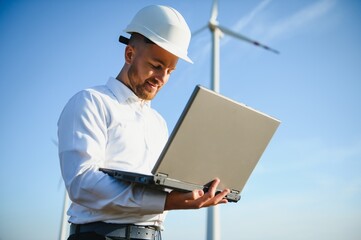 Engineer standing and hoding laptop with wind turbine.