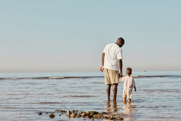 Minimal back view portrait of happy young father and son enjoying walk on beach together and...