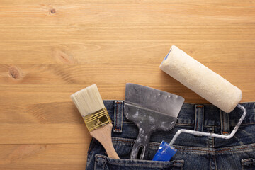 Kit of paint tool in jeans pocket at wooden table background. House renovation concept
