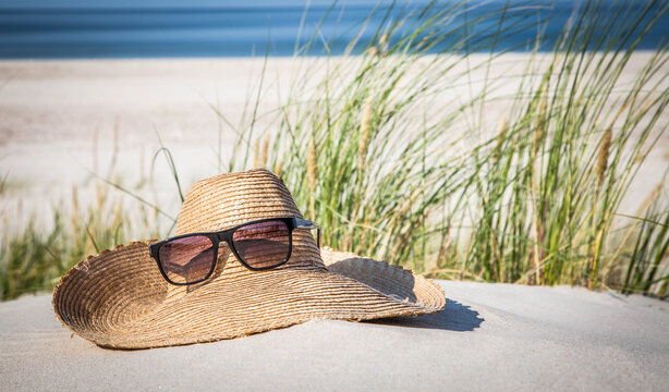Summer vibes. Sunglasses and a straw hat are lying on the beach. Holiday background.