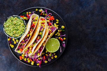 Vegetarian tacos with sweet corn, purple cabbage and tomatoes on a black plate. Tacos with vegetables and guacamole sauce on dark background. Copy space. Top view