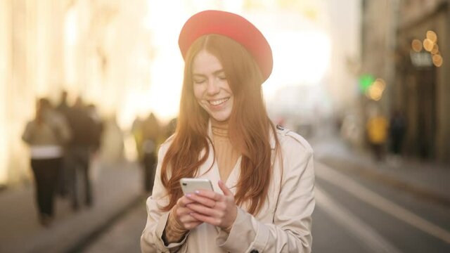 Portrait of attractive red head girl with freckles texting on her phone. Beautiful young lady at the city street. High quality 4k footage