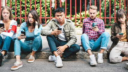 Milenial friends group using smartphone sitting at university college backyard - Young people...