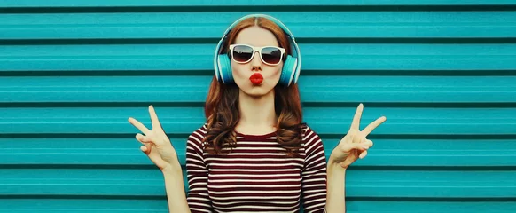Gartenposter Portrait of cheerful young woman with headphones listening to music on a colorful blue background © rohappy