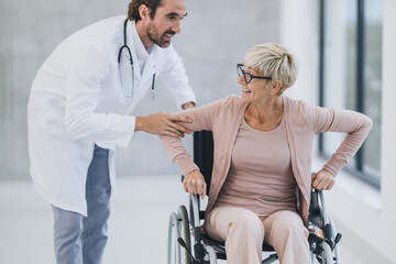Fototapeta na wymiar Senior Woman Using A Wheelchair Along The Hospital Hallway And Talking With Her Doctor