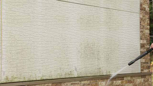Man cleaning walls with high pressure power washer. Washing cladding walls house.