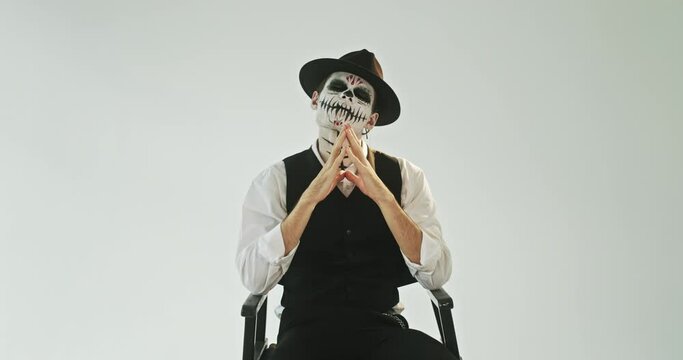 Portrait of a spooky image on Halloween makeup sugar skull man in a suit looks horrible at the camera sitting on a white background