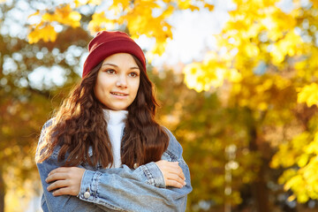 a girl in a denim jacket and a red hat freezes in the park in autumn space for text