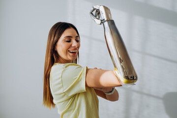 Portrait of a strong and independent woman with a bionic prosthetic arm shows a bicep on a light background looks at the camera and smiles