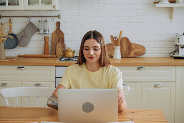 Happy young woman with modern metal bionic arm works surfing internet with laptop sitting at wooden table in kitchen closeup